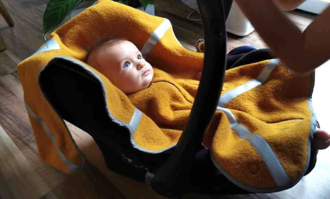 Ein sicher in der Babyschale angeschnalltes Kind unter einem Wollponcho